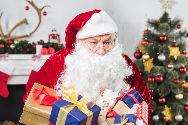 Санта с подарочными коробками возле украшенной елки