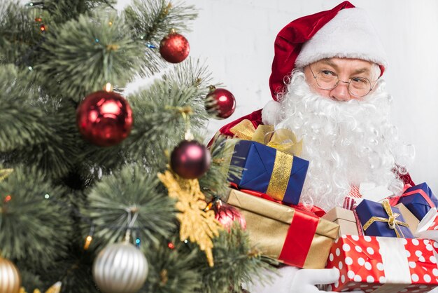 Santa with presents in hands near decorated Christmas tree