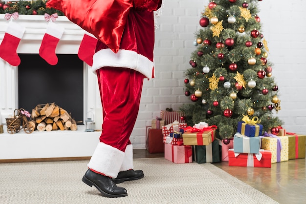 Santa with sack of gifts behind back going to Christmas tree