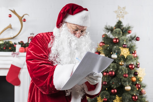 Free photo santa writing on paper near decorated christmas tree