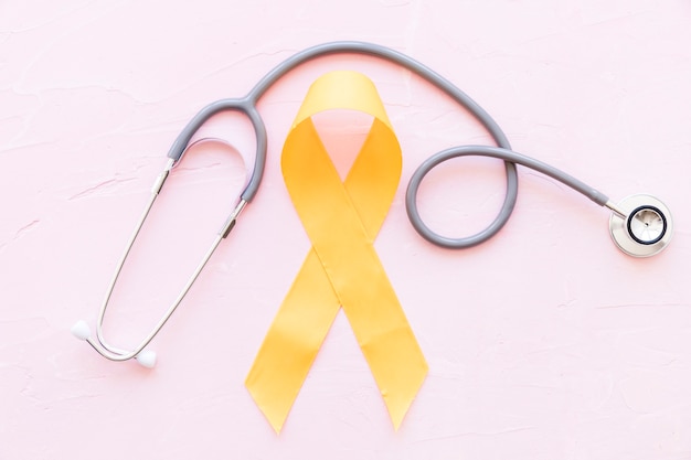 Sarcoma bone cancer yellow ribbon with stethoscope on pink background