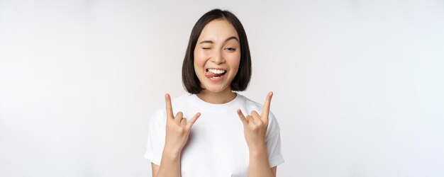 Sassy asian girl shouting enjoying concert or festival showing rock on heavy metal sign having fun standing over white background