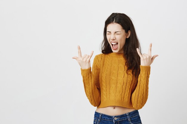 Sassy attractive brunette girl showing rock-n-roll gesture, having fun at concert