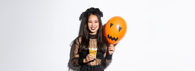 オレンジ色の風船を持ってハロウィーンを祝うトリックや治療を楽しんでいる生意気な美しいアジアの女性