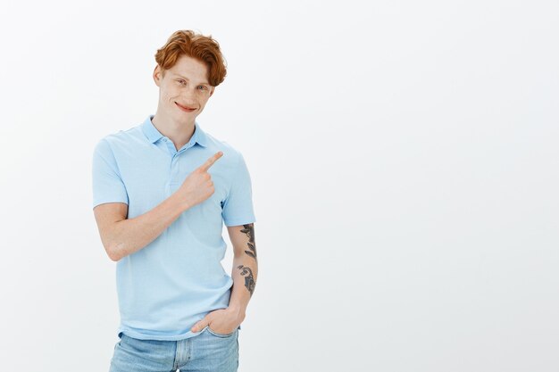 Sassy charismatic redhead man with tattoos pointing upper right corner, showing way