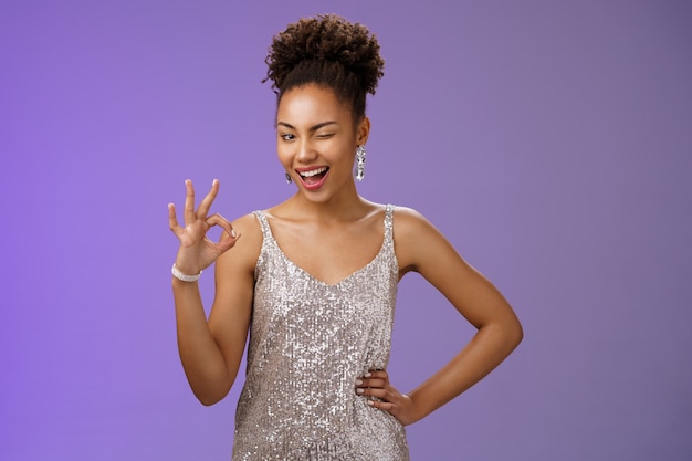 Sassy confident happy young african-american joyful girl having fun winking cheeky smiling camera show okay excellent ok gesture satisfied perfect results recommend service, blue background.