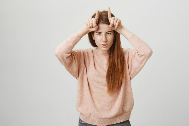 Sassy cute redhead girl showing devil horns on head