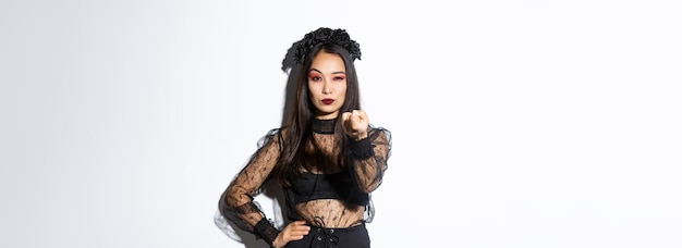 Sassy elegant young asian woman in witch halloween costume tell come closer flicking finger as lure