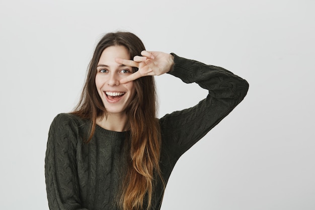 Sassy good-looking woman showing peace sign and smiling confident