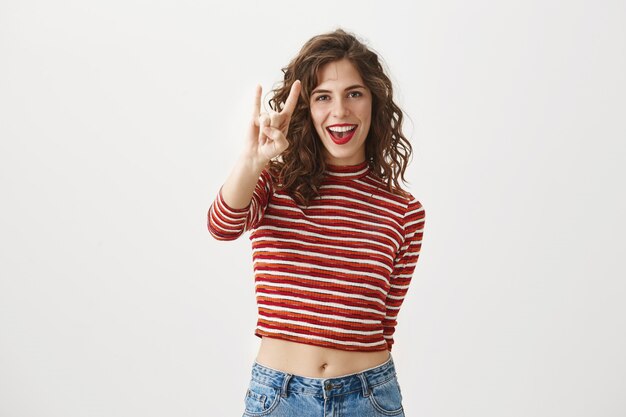 Sassy good-looking woman smiling and showing rock-n-roll gesture