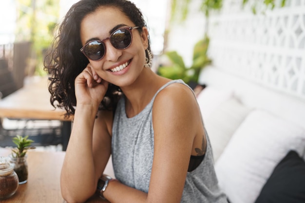 Free photo sassy goodlooking woman dark curly haircut wear glasses sitting summer patio cafe tilt head flirty smiling laughing intrigued listen story romantic date relaxing enjoying tropical hotel resort