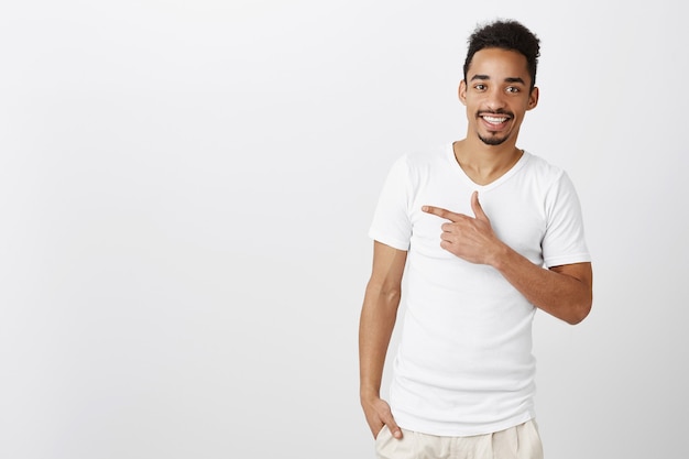 Free photo satisfied african american guy pointing upper left corner with confident smile