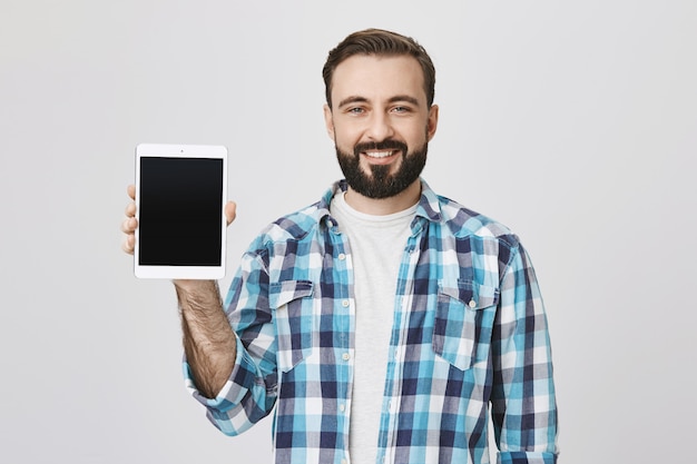 Free photo satisfied bearded man showing digital tablet screen, smiling
