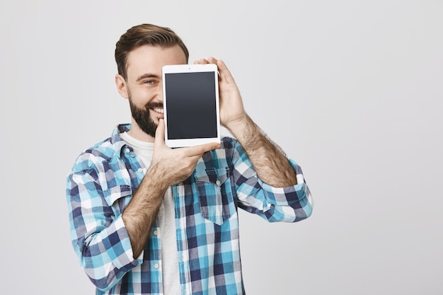 Foto gratuita uomo barbuto soddisfatto che mostra lo schermo della tavoletta digitale, sorridente
