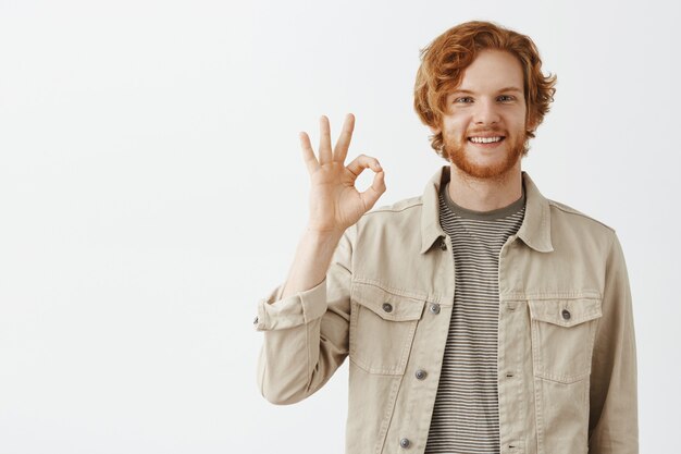 Satisfied bearded redhead guy posing against the white wall