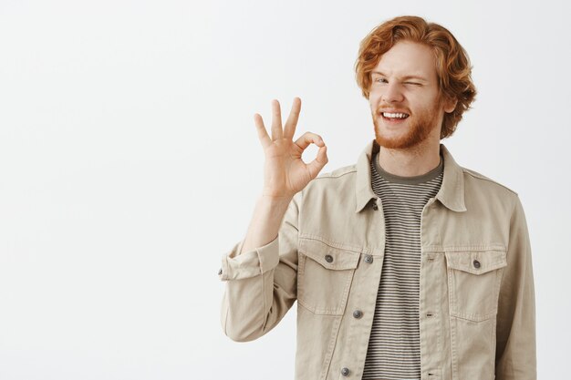 Satisfied bearded redhead guy posing against the white wall