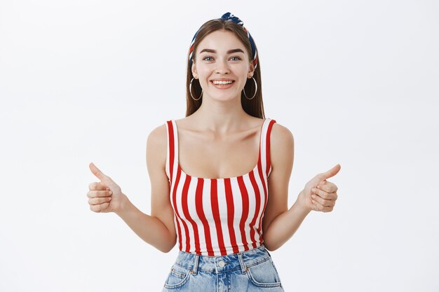 Satisfied beautiful slim woman in striped pin-up style top and headband smiling broadly showing thumbs up