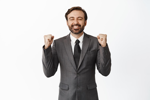 Foto gratuita uomo d'affari soddisfatto che si rallegra celebrando la vittoria sorridendo soddisfatto e chiudendo gli occhi dalla soddisfazione trionfando in piedi su sfondo bianco