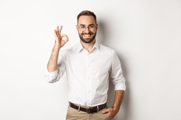Satisfied businessman smiling and showing ok sign, approve and like something good, standing  