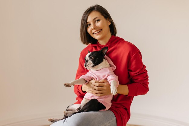 Satisfied caucasian young woman with smile on her face holds dog while sitting on white background Lifestyle and friendship concept