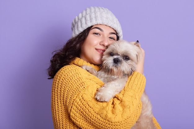 Satisfied dark haired female with her puppy looks at camera with cute facial expression