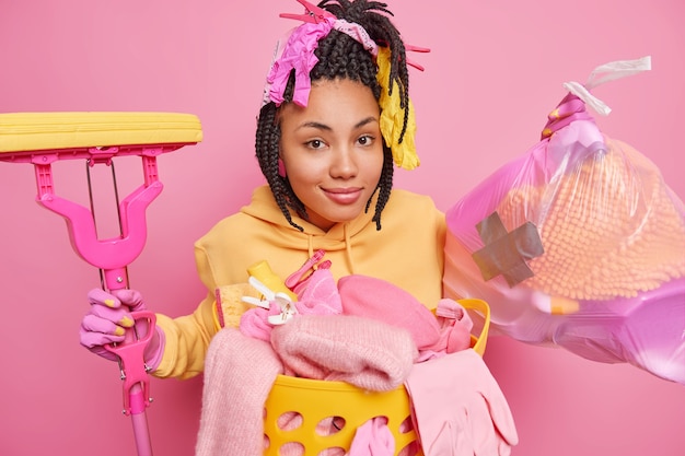 Satisfied ethnic woman with rubber gloves on braids holds litter bag