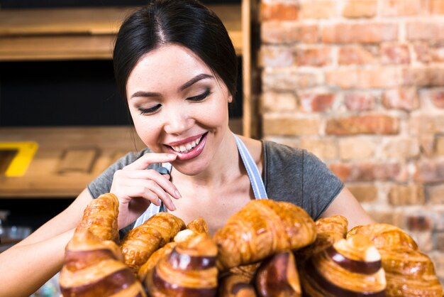 Удовлетворенная женщина-пекарь смотрит на свежеиспеченный круассан