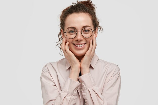 satisfied freckled teenager with glasses posing against the white wall