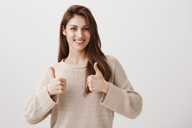 Satisfied girl showing well done thumbs-up gesture, smiling pleased