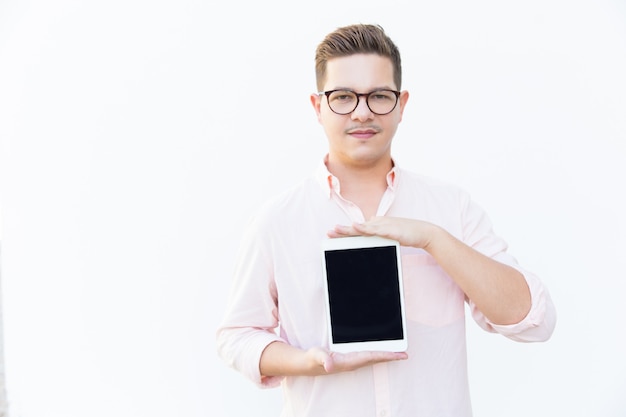 Satisfied guy in eyeglasses presenting blank tablet screen