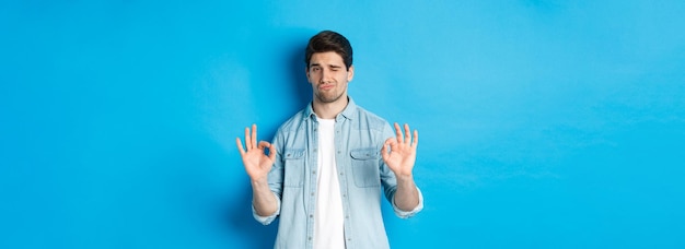 Free photo satisfied handsome man showing aok signs and looking pleased approving something good standing again