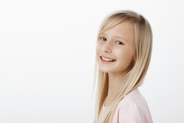 Foto gratuita soddisfatta felice bambina caucasica con lunghi capelli biondi, sorridendo allegramente