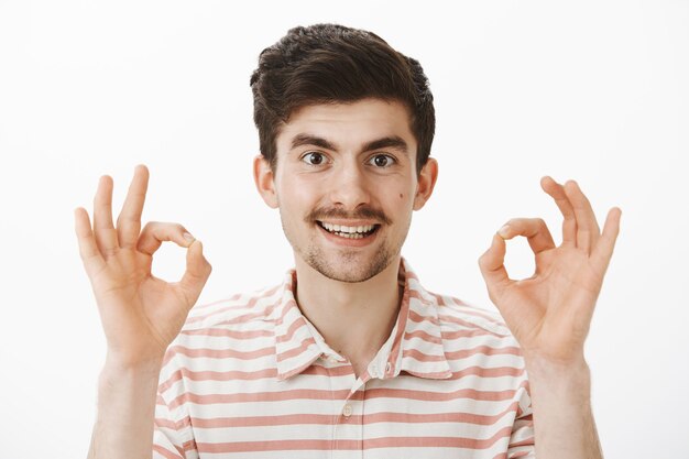 satisfied interested attractive man with moustache, raising fingers and showing ok or okay gesture, approving great suggestion, happy to solve problem, have everything under control