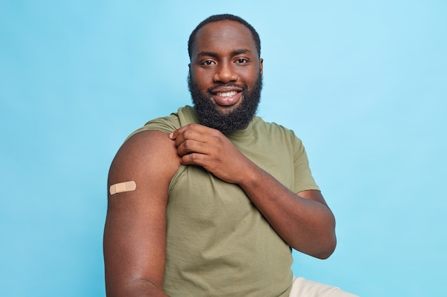 Free photo satisfied man after vaccination shows adhesive bandage on arm got covid 19 vaccination to cure disease isolated over blue wall