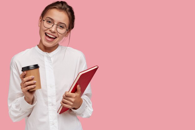 Satisfied pretty smiling young woman in spectacles, carries takeaway coffee