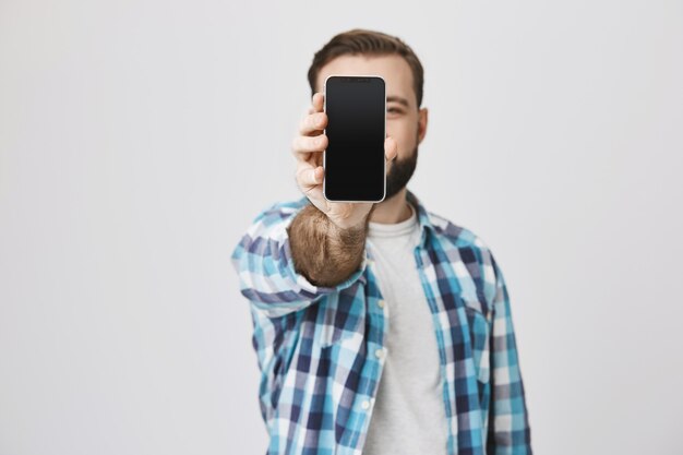 Satisfied smiling bearded man showing smartphone screen, application promo