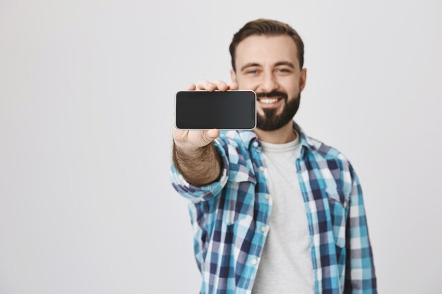 Satisfied smiling bearded man showing smartphone screen, application promo