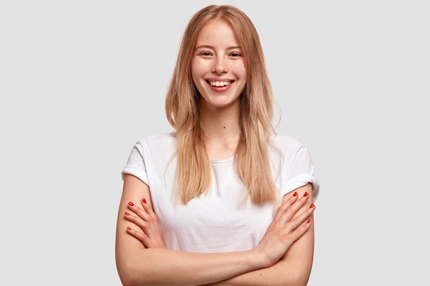 Satisfied smiling blonde young woman with pleased expression, expresses happiness, dressed in casual white t shirt