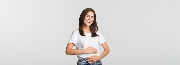 Free photo satisfied smiling brunette girl rubbing belly after eating delicious food