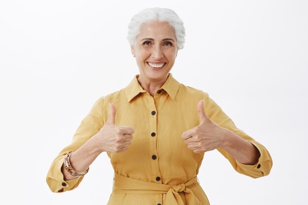 Satisfied smiling senior woman showing thumbs-up in approval, white background