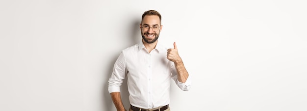 Бесплатное фото Удовлетворенный успешный босс, показывающий большой палец вверх, одобряет и хвалит хорошую работу, стоя над белым му