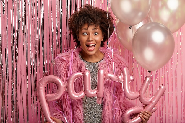 Free photo satisfied surprised female with afro hairstyle holds balloons, sees many old friends on party