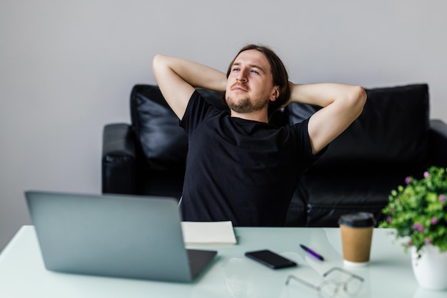 Free photo satisfied with work done happy young man working on laptop while sitting at his working place in office