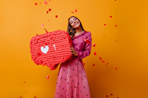 Satisfied woman in pink outfit laughing. Adorable caucasian girl in long skirt standing on yellow wall.