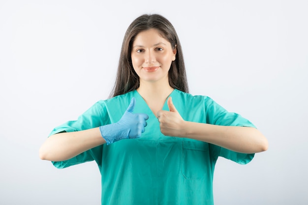 親指を立てて医療用手袋で満足した若い女性医師。