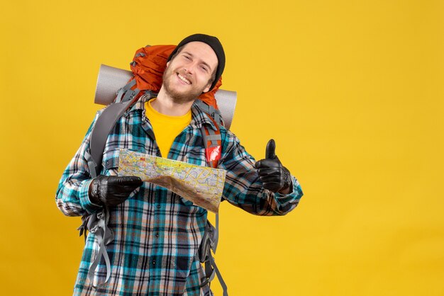 satisfied young tourist with leather gloves and backpack holding map giving thumb up