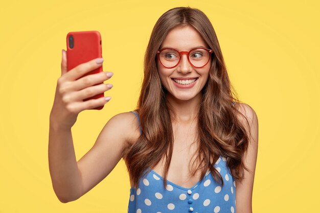 Satisfied young woman with glasses posing against the yellow wall