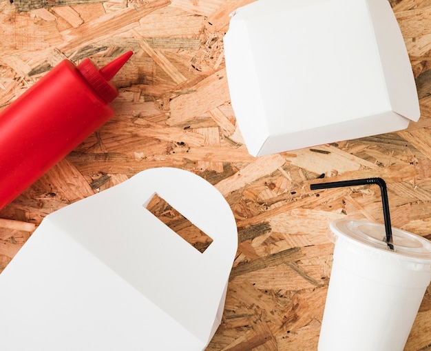 Sauce bottle; white package and disposable drink on wooden backdrop