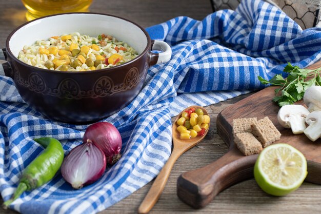 A saucepan of noodles with vegetables and spoon on tablecloth