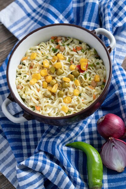 A saucepan of noodles with vegetables on tablecloth